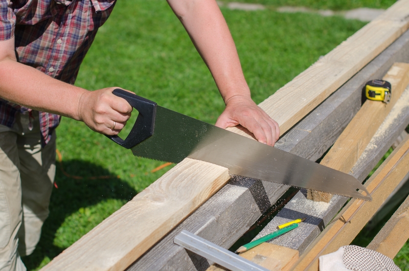 5900154-handyman-sawing-long-wooden-plank-outdoors